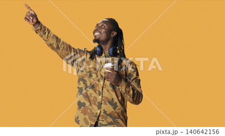 Casual person drinking coffee cup on camera, enjoying hot caffeine beverage in studio, with male model posing with refreshment and smiling over orange background. 140642156