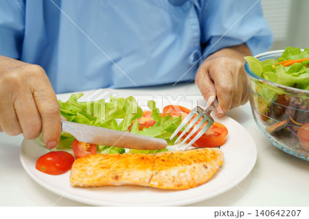 Asian elderly woman patient eating salmon stake and vegetable salad for healthy food in hospital. 140642207