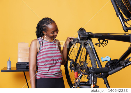 Dedicated woman checking bicycle tires for damages to fix with professional work tools. 140642288