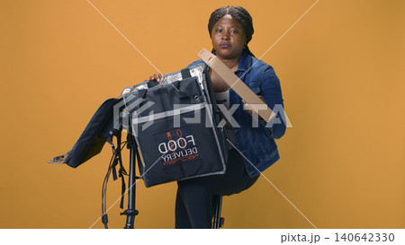 Woman on bicycle carefully delivering fresh takeout meal with courier bag, with delivery person providing professional customer service by making efficient delivery. Woman on bicycle carefully delivering fresh takeout meal with courier bag, with delivery person providing professional customer service by making efficient delivery. 140642330