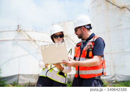 Male and female industrial engineers using laptop at oil refinery Male and female industrial engineers using laptop at oil refinery 140642380