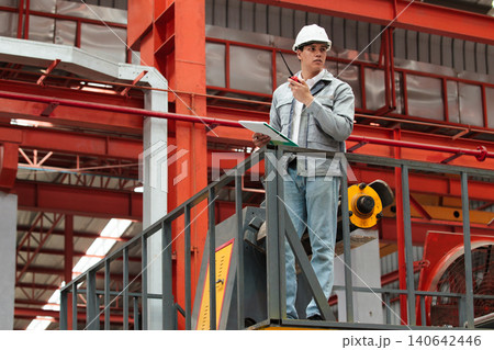 Hispanic male engineer communicating with radio in factory Hispanic male engineer communicating with radio in factory 140642446