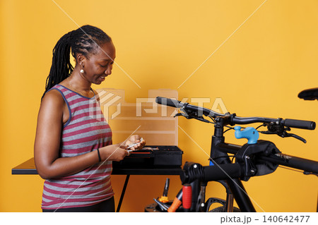 Sports-loving woman choosing and examining different tools from professional toolbox for bike maintenance, with female cyclist grasping specialized equipment for repairing bicycle. Sports-loving woman choosing and examining different tools from professional toolbox for bike maintenance, with female cyclist grasping specialized equipment for repairing bicycle. 140642477