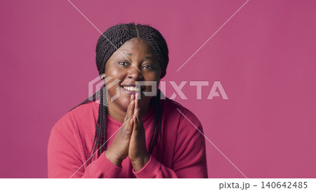 Stunning woman looks at the camera while really pleading with her hands together, with young female with appealing and requesting body language in front of pink background. Stunning woman looks at the camera while really pleading with her hands together, with young female with appealing and requesting body language in front of pink background. 140642485