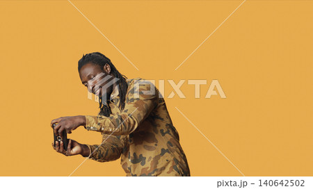 Cheerful adult playing rpg videogames on mobile gadget, having fun with gaming competition on smartphone in studio, with man enjoying shooting game with people, orange background. 140642502