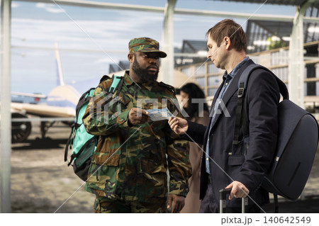 Airport traveler in camouflage clothing helped my man to understand boarding pass flight information. Army soldier wearing backpack asking businessman about plane ticket Airport traveler in camouflage clothing helped my man to understand boarding pass flight information. Army soldier wearing backpack asking businessman about plane ticket 140642549