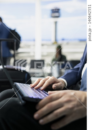 Close up of entrepreneur works on laptop before departure in airport terminal, frequent flyer corporate travel. CEO traveler near gate with luggage ready, international flight departure. Close up of entrepreneur works on laptop before departure in airport terminal, frequent flyer corporate travel. CEO traveler near gate with luggage ready, international flight departure. 140642551