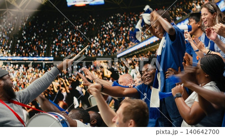 Blue soccer supporters cheering together in crowded stadium during live football match in the supporter section. Passionate sports fans celebrate together, crowd cheering and nonstop fan chants. Blue soccer supporters cheering together in crowded stadium during live football match in the supporter section. Passionate sports fans celebrate together, crowd cheering and nonstop fan chants. 140642700