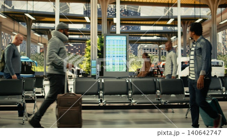 Busy bus station platform with travelers preparing for intercity long-haul trip. Passengers carrying carry-on trolley bags checking departure board timetable and route before coach journey. Busy bus station platform with travelers preparing for intercity long-haul trip. Passengers carrying carry-on trolley bags checking departure board timetable and route before coach journey. 140642747