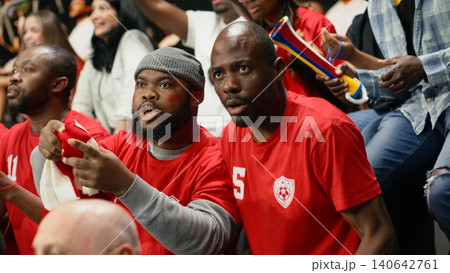 Football fan celebrating winning goal during live match in the stadium stands, crowd celebration for world champions. Multigenerational supporters cheering together with raised fists. Football fan celebrating winning goal during live match in the stadium stands, crowd celebration for world champions. Multigenerational supporters cheering together with raised fists. 140642761