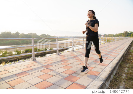 Active Asian woman running outdoors along a riverside walkway. Active Asian woman running outdoors along a riverside walkway. 140642774