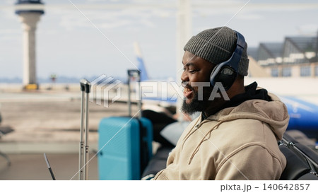 African american man on video conference call using airport internet, speaking to colleagues during online meeting while seated in the terminal waiting area. Digital communication and mobility. African american man on video conference call using airport internet, speaking to colleagues during online meeting while seated in the terminal waiting area. Digital communication and mobility. 140642857