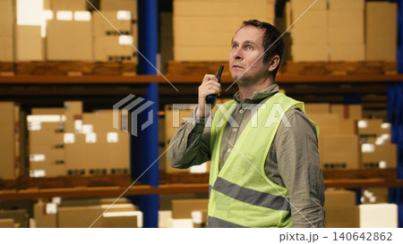 Warehouse operator reporting parcel status via two-way portable transceiver, ensuring teamwork through radio signal walkie-talkie in depot. Professional communication ensures order fulfillment. 140642862