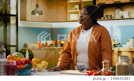 Portrait of african american woman smiling and filming online tutorial in home kitchen studio, creating gourmet dish with fresh ingredients and cooking process. Content creator home chef. Portrait of african american woman smiling and filming online tutorial in home kitchen studio, creating gourmet dish with fresh ingredients and cooking process. Content creator home chef. 140642867