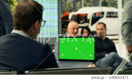 Green screen mockup with person seated inside busy bus terminal using laptop. Isolated chroma key on pc surrounded by commuters and urban transit activity, metropolitan public transportation. 140642871