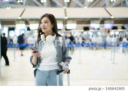Asian woman traveler with suitcase using smartphone at airport check-in Asian woman traveler with suitcase using smartphone at airport check-in 140642905