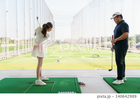 Woman learning golf swing technique with a coach at a driving range. Woman learning golf swing technique with a coach at a driving range. 140642989