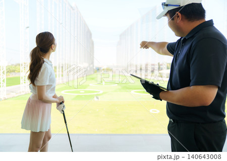 Golf instructor explaining swing technique on digital tablet to woman golfer at driving range. Golf instructor explaining swing technique on digital tablet to woman golfer at driving range. 140643008
