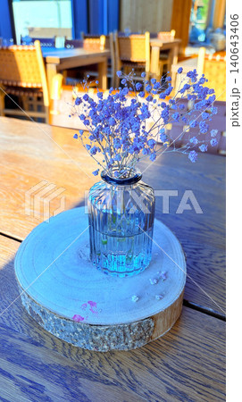 Minimalist Glass Vase with Dried Babys Breath Flowers on Wooden Table in Cozy Cafe Interior 140643406