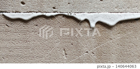 A textured concrete wall that has a rough surface and irregular white sealant lines that run horizontally along the frame. 140644063