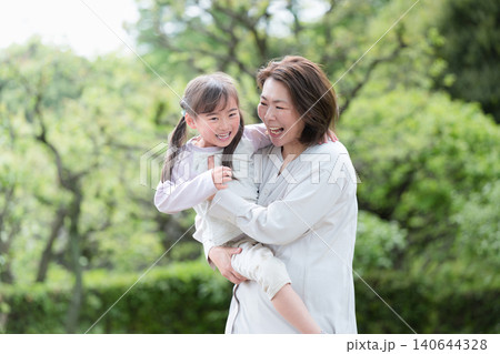 新緑の公園で母親に抱っこされるスキンシップな笑顔の女の子 親子愛と幸せな家族時間 新緑の公園で母親に抱っこされるスキンシップな笑顔の女の子 親子愛と幸せな家族時間 140644328