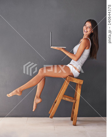 Laptop, portrait and woman on chair to balance in studio with gray wall background for social media. Computer, smile and underwear with happy young person on stool to relax for blogging or streaming Laptop, portrait and woman on chair to balance in studio with gray wall background for social media. Computer, smile and underwear with happy young person on stool to relax for blogging or streaming 140644378