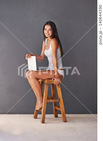 Laptop, portrait and smile of woman on chair in studio with gray wall background for social media. Computer, relax and underwear with happy young person sitting on stool for blogging or streaming Laptop, portrait and smile of woman on chair in studio with gray wall background for social media. Computer, relax and underwear with happy young person sitting on stool for blogging or streaming 140644390