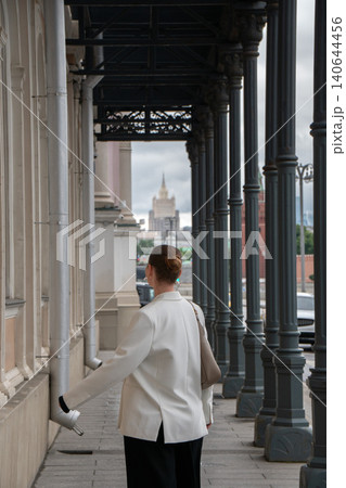 Woman walks through colonnade on Sofiyskaya Embankment in Moscow, dark columns, distant Stalinist skyscraper, urban perspective, contemporary city atmosphere. Travel, urban lifestyle, destination Woman walks through colonnade on Sofiyskaya Embankment in Moscow, dark columns, distant Stalinist skyscraper, urban perspective, contemporary city atmosphere. Travel, urban lifestyle, destination 140644456