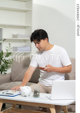 Concept with saving money, man working on desk in home using calculator and laptop to calculate budget. Concept with saving money, man working on desk in home using calculator and laptop to calculate budget. 140644823