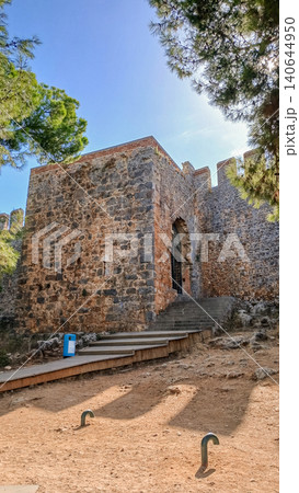 Ancient stone fortress entrance surrounded by trees and blue sky in Alanya, Turkey Ancient stone fortress entrance surrounded by trees and blue sky in Alanya, Turkey 140644950