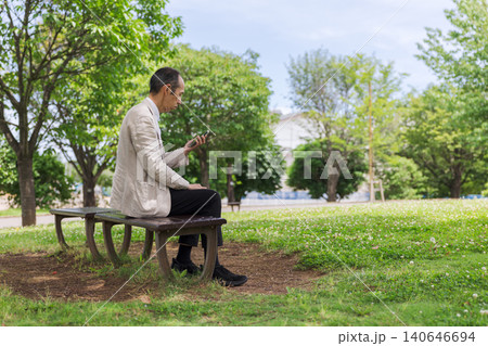 公園のベンチでスマートフォンを見る日本人男性 140646694