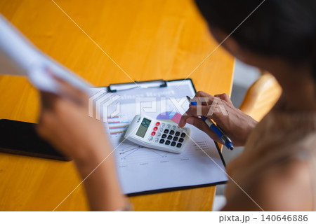 Overhead business scene with calculator, pen, and financial report on a desk, showing budget calculation, accounting review, tax planning, expense analysis, corporate paperwork, and office work. Overhead business scene with calculator, pen, and financial report on a desk, showing budget calculation, accounting review, tax planning, expense analysis, corporate paperwork, and office work. 140646886