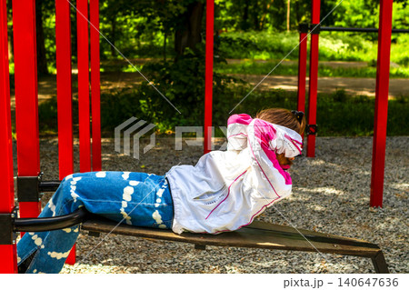 Young girl doing outdoor core exercise on a bench in a park during sunny day Young girl doing outdoor core exercise on a bench in a park during sunny day 140647636
