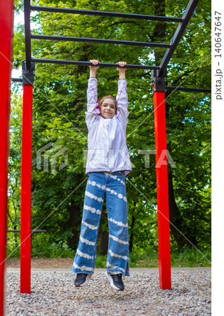 Young girl hanging from monkey bars at outdoor playground showing strength, play and joyful movement in park 140647647