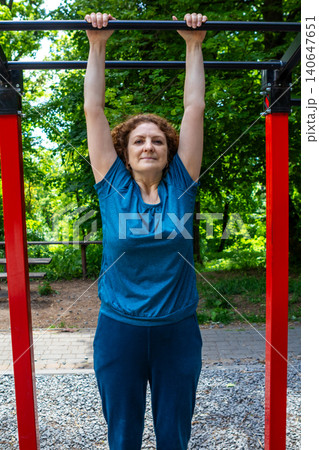 Mature woman doing pullup exercise on outdoor bar in park demonstrating fitness and strength 140647651