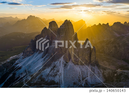 Panoramic view of Tre Cime di Lavaredo glowing in golden sunset light in the Italian Dolomites. Dramatic alpine landscape with rugged peaks, winding trails and breathtaking scenery. Panoramic view of Tre Cime di Lavaredo glowing in golden sunset light in the Italian Dolomites. Dramatic alpine landscape with rugged peaks, winding trails and breathtaking scenery. 140650143