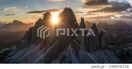 Spectacular sunset over Tre Cime di Lavaredo in the Italian Dolomites. Golden sunburst shines between iconic limestone peaks, creating a dramatic alpine mountain landscape. Spectacular sunset over Tre Cime di Lavaredo in the Italian Dolomites. Golden sunburst shines between iconic limestone peaks, creating a dramatic alpine mountain landscape. 140650158