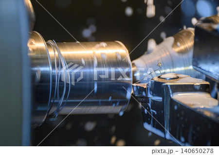 Close-up of a lathe machine performing a precision finishing cut on a metal shaft with liquid coolant. Close-up of a lathe machine performing a precision finishing cut on a metal shaft with liquid coolant. 140650278
