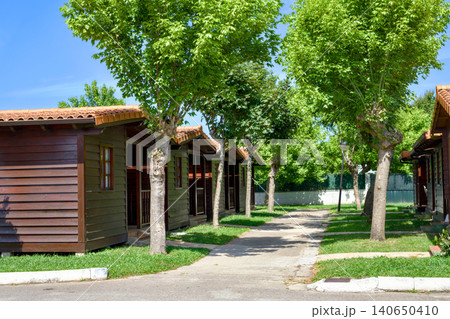 Row of Wooden Eco Bungalows Along Shaded Pathway at Summer Resort Row of Wooden Eco Bungalows Along Shaded Pathway at Summer Resort 140650410