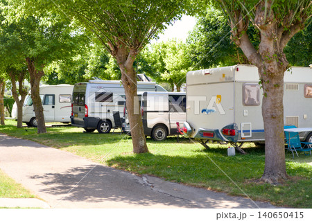 RV Campers and Caravans Parked in Green Campground With Tall Trees RV Campers and Caravans Parked in Green Campground With Tall Trees 140650415
