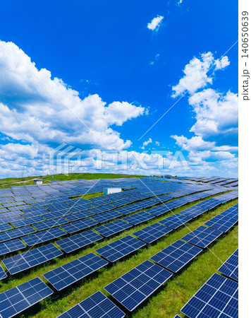 Sunlit fields with multiple solar panels. Sprawling photovoltaic arrays shine brightly amid lush green countryside beneath sky filled with billowing clouds and intense sunlight Sunlit fields with multiple solar panels. Sprawling photovoltaic arrays shine brightly amid lush green countryside beneath sky filled with billowing clouds and intense sunlight 140650639