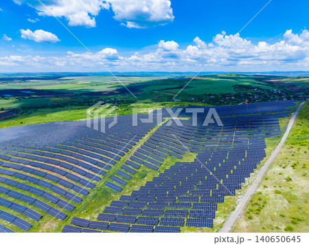 Solar farm landscape. Bright blue sky over sprawling photovoltaic field complex. Modern renewable energy project showcasing solar array array amidst lush green surroundings Solar farm landscape. Bright blue sky over sprawling photovoltaic field complex. Modern renewable energy project showcasing solar array array amidst lush green surroundings 140650645