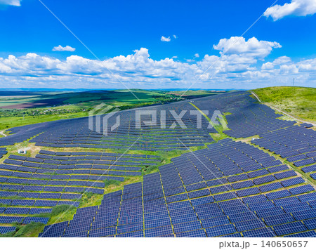 Photovoltaic field contouring rugged hillside with grassy pathways. Aerial perspective of solar panels on steep terrain with natural greenery and reflective surfaces Photovoltaic field contouring rugged hillside with grassy pathways. Aerial perspective of solar panels on steep terrain with natural greenery and reflective surfaces 140650657