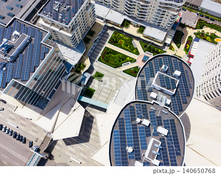 Solar panels cover rooftops in a modern urban setting with green spaces and walkways during the day 140650768