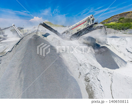Granite quarry operations take place in a remote area with heavy machinery processing stone during midday under clear skies 140650811