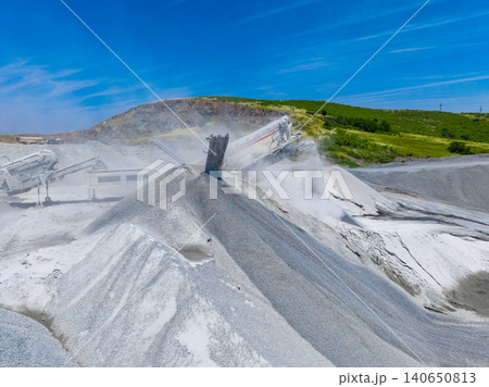 Operations at granite quarry show heavy machinery working on stone extraction and material processing under clear blue sky Operations at granite quarry show heavy machinery working on stone extraction and material processing under clear blue sky 140650813