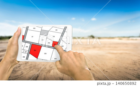 Man holding a tablet looking at lots of lands. Land plot management - real estate concept with vacant land for building construction and housing subdivision for sale, rent, buy, or investment. Man holding a tablet looking at lots of lands. Land plot management - real estate concept with vacant land for building construction and housing subdivision for sale, rent, buy, or investment. 140650892