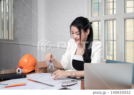 Female architect using dividers working on blueprint architects project in office. Female architect using dividers working on blueprint architects project in office. 140650932