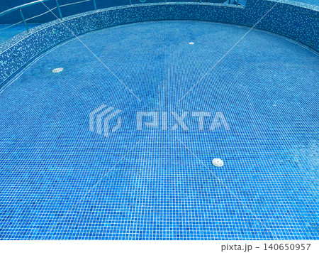 Water fills a round swimming pool with blue tiles and a clean floor on a sunny day in a resort location during summer afternoons Water fills a round swimming pool with blue tiles and a clean floor on a sunny day in a resort location during summer afternoons 140650957
