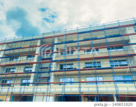 Construction work is ongoing on a multi-story building with scaffolding around it in a city during the day under a cloudy sky Construction work is ongoing on a multi-story building with scaffolding around it in a city during the day under a cloudy sky 140651020